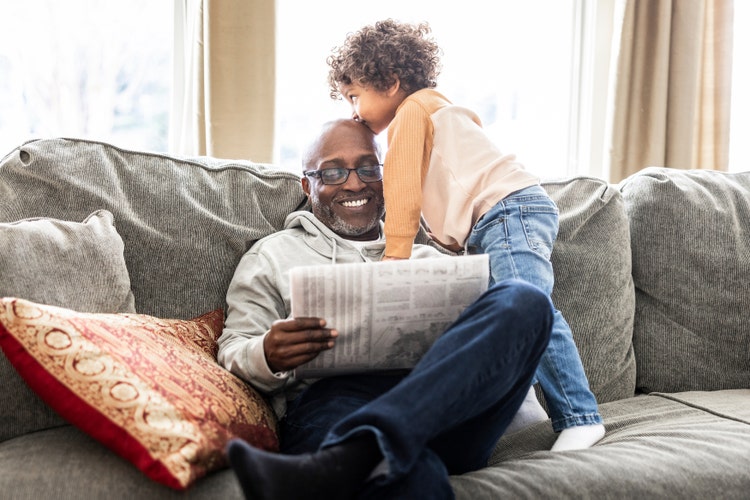 Older man on couch reading newspaper with grandson