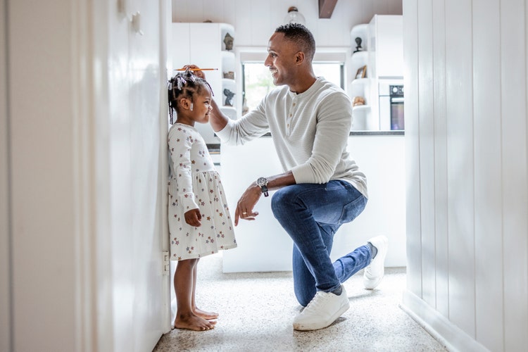 A man measures the height of a young girl standing against a doorway
