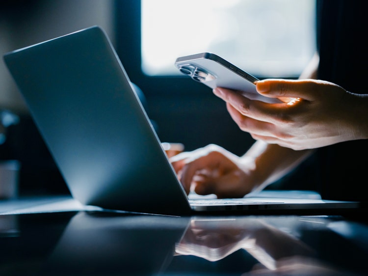 person holding a phone in hand while using a laptop