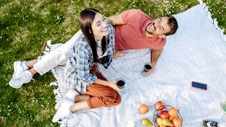 A man and woman sit on a picnic blanket
